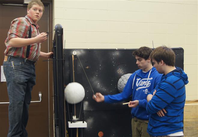 Harrison Fangmann (left) paints Project Lead the Way's Rube Goldberg machine while Patrick Jenson (middle) demonstrates the parachute system to Mitchell Merz (left).
