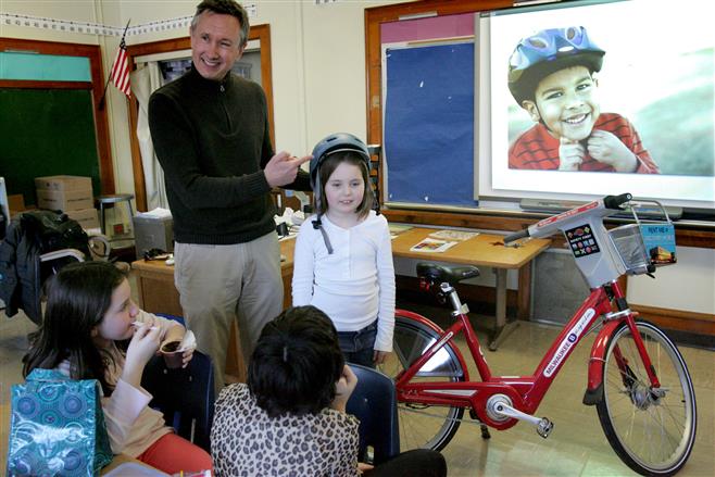 Fourth-grader Nora Pionek helps Kevin Hardman demonstrate the proper way to fit a helmet during his Brown Bag Lunch presentation about his career path. He promotes bicycling and the Milwaukee BikeShare program. About 30 fourth- and fifth-grade students at Lincoln Elementary School listened to his talk Feb. 25.