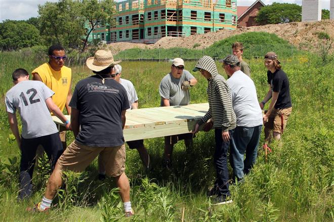 Spencer Zuberbuehler (background, second from right) gets help from friends and troop leaders to install a footbridge in a monarch reserve on Innovation Campus in Wauwatosa on June 21. Staff photo by Rory Linnane.