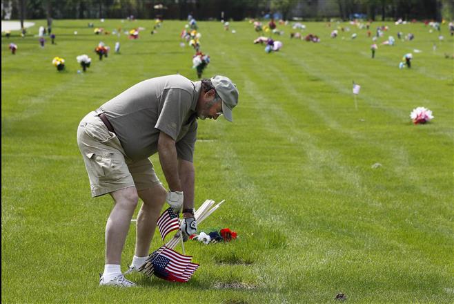 Terry King, of Wauwatosa, places a flag at the headstone of a veterans grave at Graceland Cemetery on Sherman Blvd. in Milwaukee on Monday, May 19, 2014. King, an army veteran who served from 1963-1965 in Germany, was volunteering with Graceland Cemetery in placing the flags in time for Memorial Day weekend.