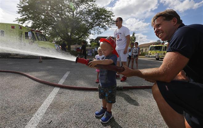 With the help of Wauwatosa firefighter Christopher Schultz, Owen High, 2  1/2 tries his hand at operating a fire hose at last year’s Night Out in Wauwatosa.