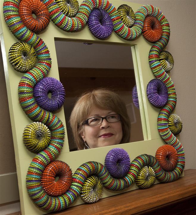 Suzanne Zakry's reflection in a mirror she made. Her husband, Dennis, makes the frame and she creates the design and embellishes it with bottlecaps.