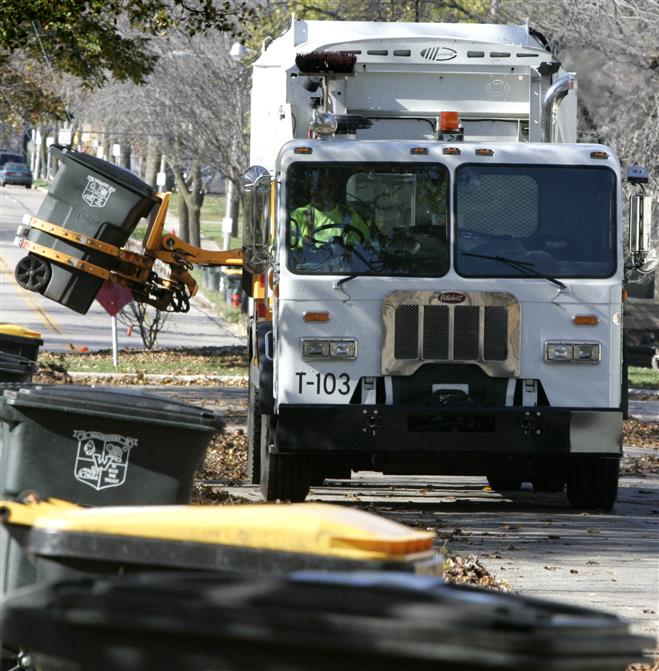 A new Wauwatosa garbage truck uses an articulated arm to reach out and grasp residential trash carts left at curbside along Chestnut Street.