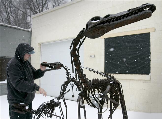Gary Kandziora cleans snow out of the jaws and eye sockets of three dinousaurs he created from scrap steel in front of his Intuitive Sculpture Studio.